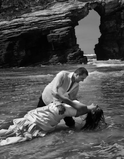 novio sujeta a su pareja en la orilla mientras la melena de ésta se moja en el mar