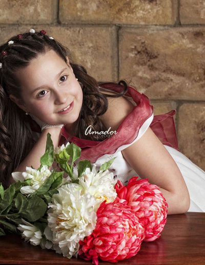 niña con vestido de comunión apoyada en una mesa coon flores