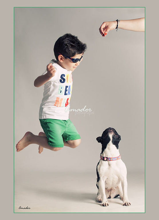 niño con camiseta, pantalón corto y gafas de sol  saltando al lado de un perro