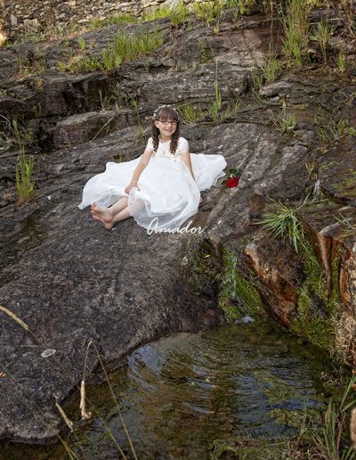 niña sentada en las rocas junto al rio con vestido de comunión
