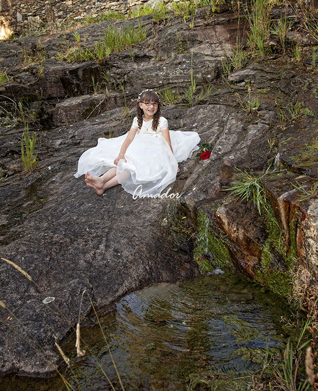 Nena con vestido de comunión sentada ao carón do río.