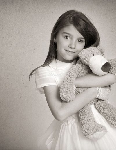 foto de estudio de niña con vestido de comunión abrazando a un oso de peluche